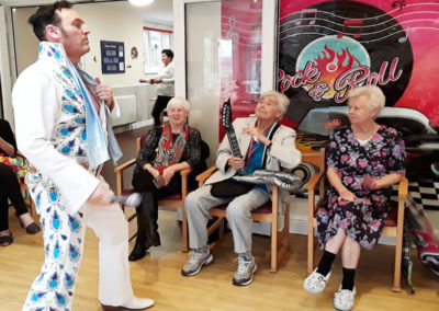 Elvis tribute singer in a white jumpsuit singing for residtents at The Old Downs Residential Care Home