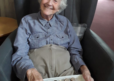 A lady resident from The Old Downs, smiling with a box of chocolates on her lap