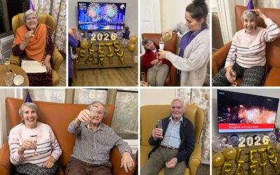 Residents at The Old Downs Residential Care Home celebrating New Year’s Eve together, raising glasses and wearing party hats, with festive decorations and a “2026 Let’s Party” display in the background.